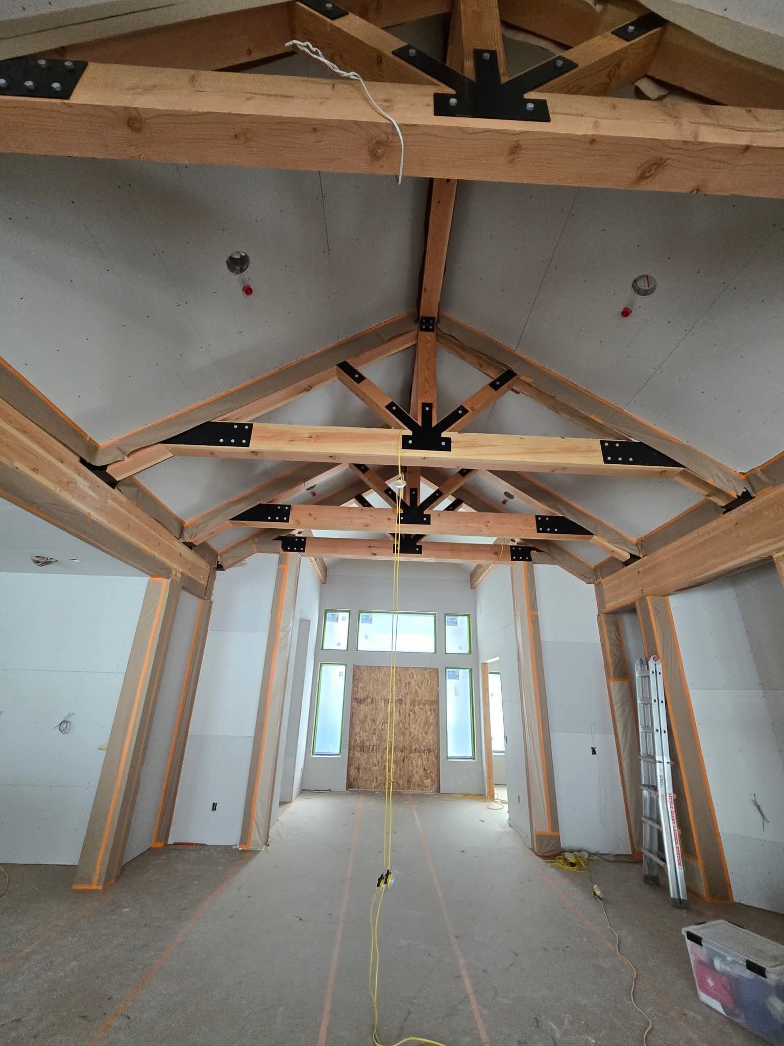 Large room with exposed timber trusses and drywall being hung — craftsmanship in progress