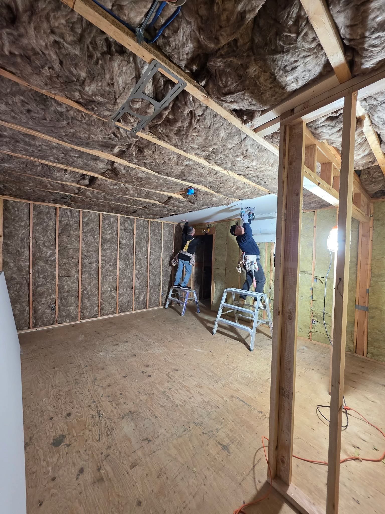 Workers installing drywall on ceiling with ladders — Tapetech team at work